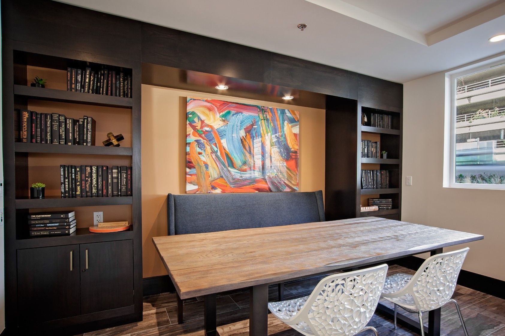 Modern conference room with wooden table, white chairs, built-in shelves, and colorful wall art