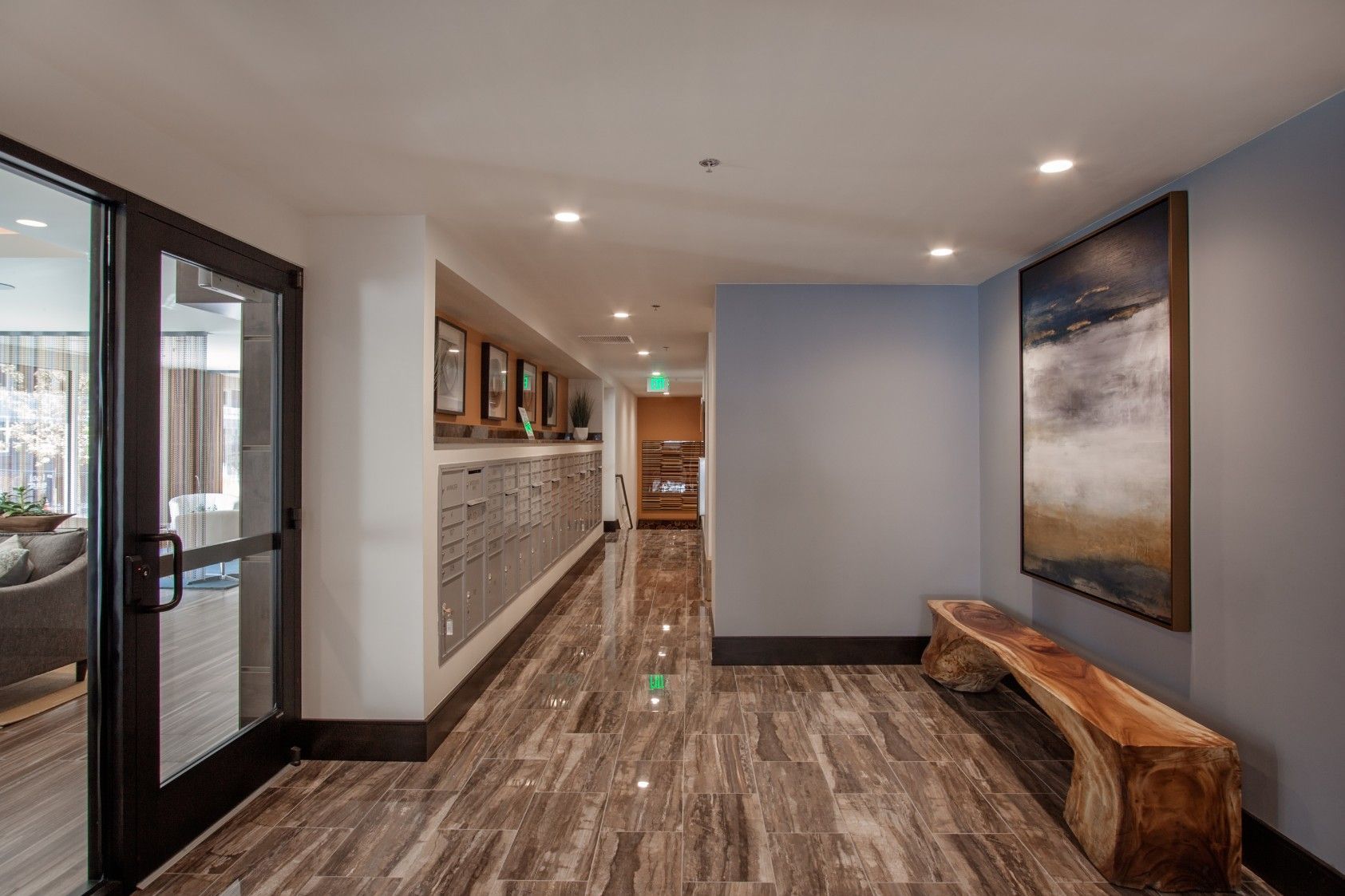 Modern office hallway with wood floors, glass doors, and a bench beneath wall art