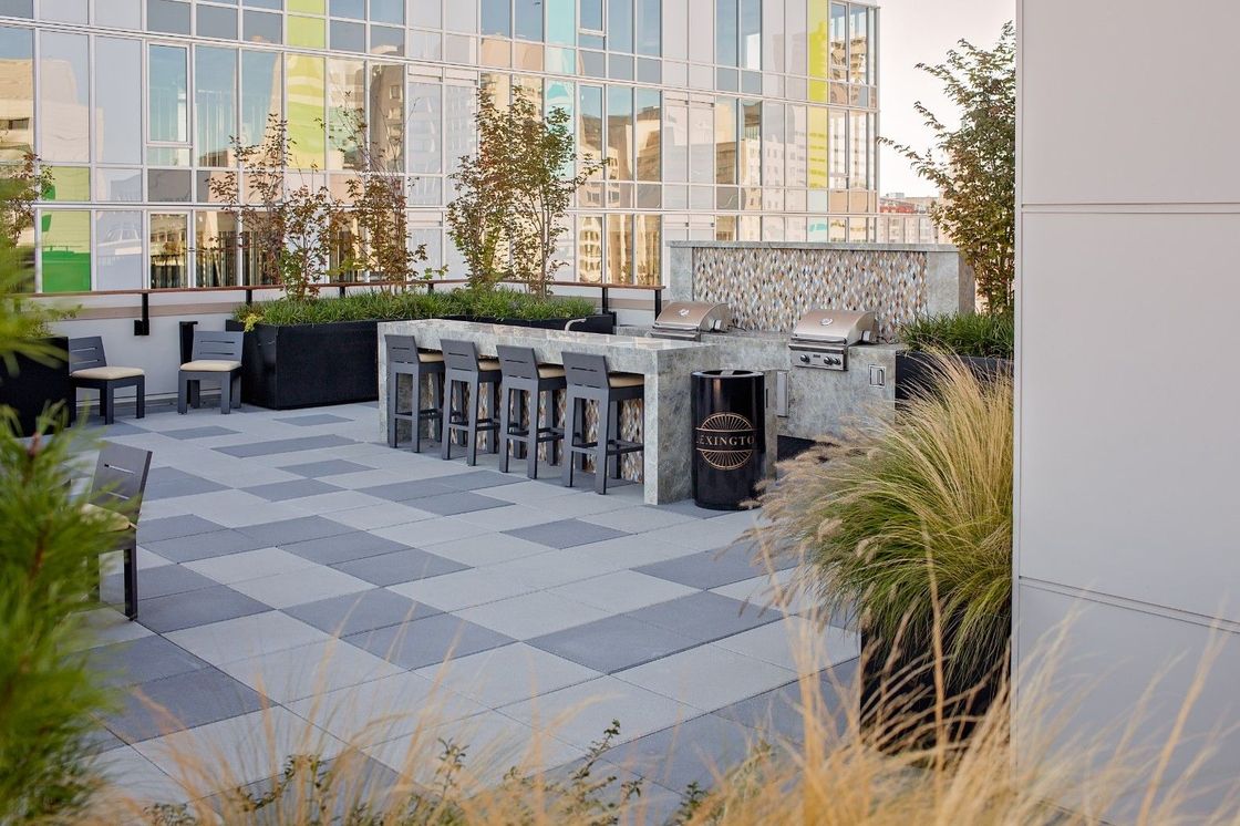 Outdoor patio with patterned pavers, bar stools, and tables beside a modern glass building.