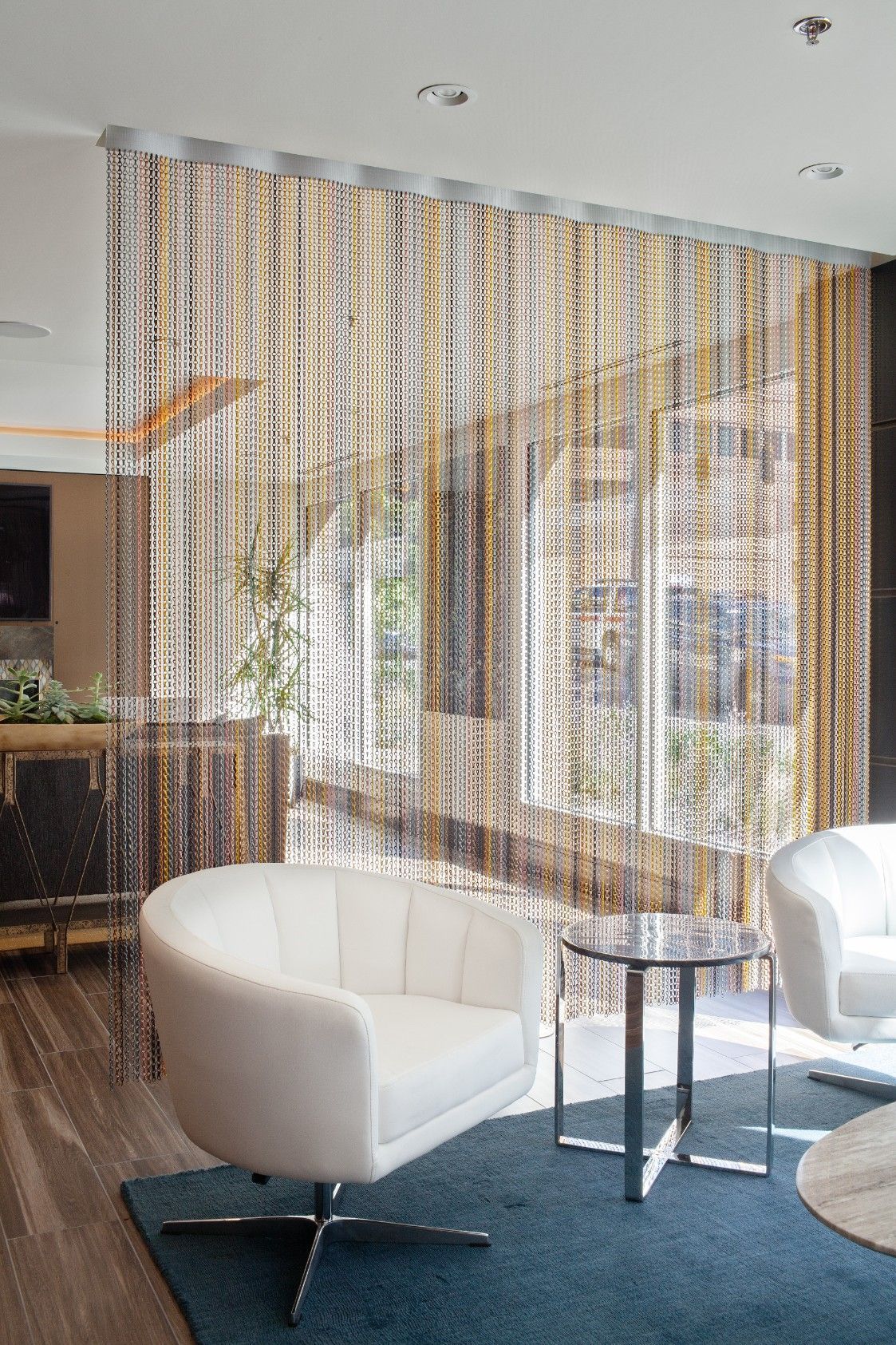 Modern living room with white chairs, round glass table, and hanging bead curtain divider