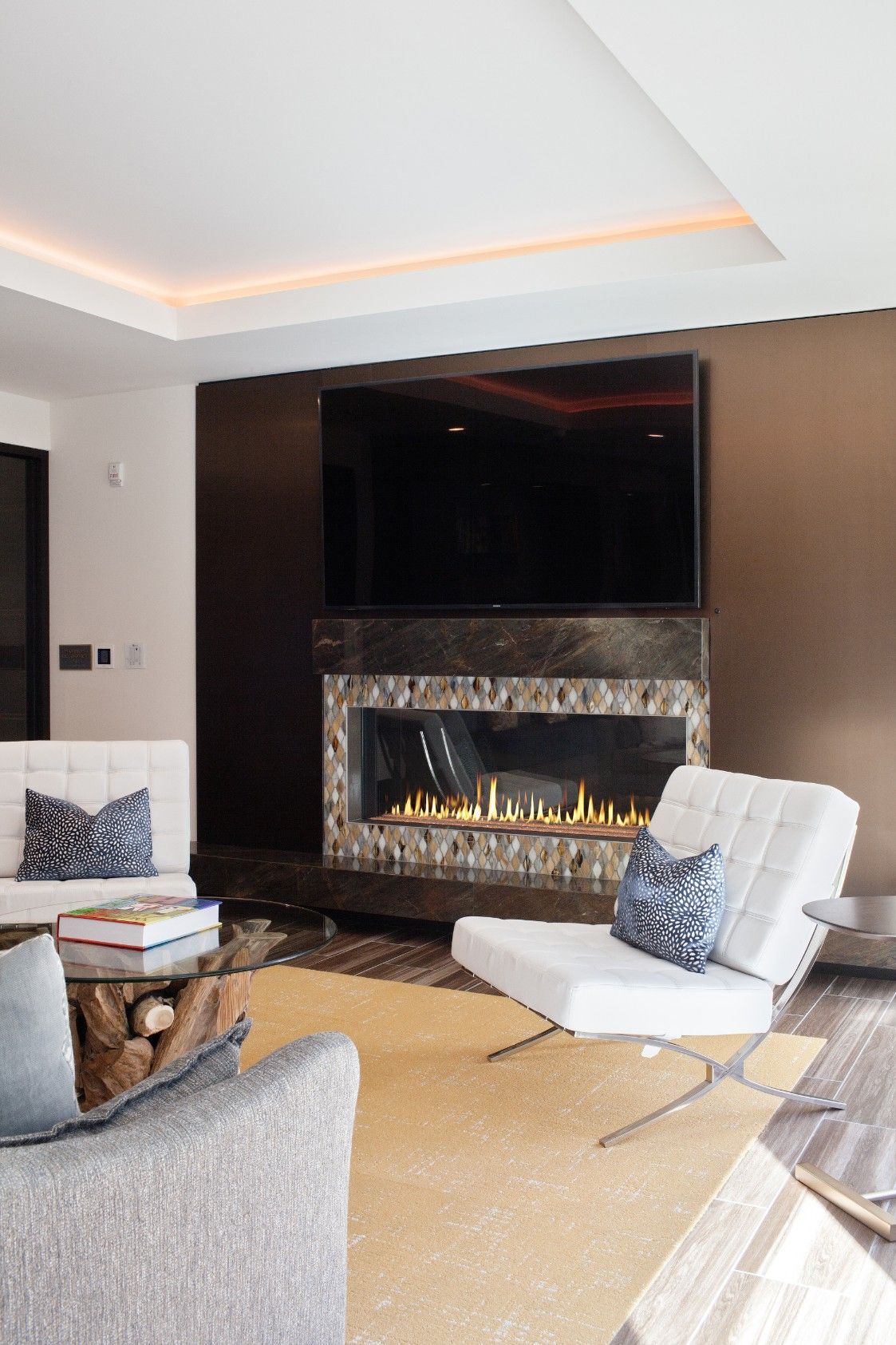 Modern living room with a wall-mounted TV, lit fireplace, and white lounge chair on a rug.