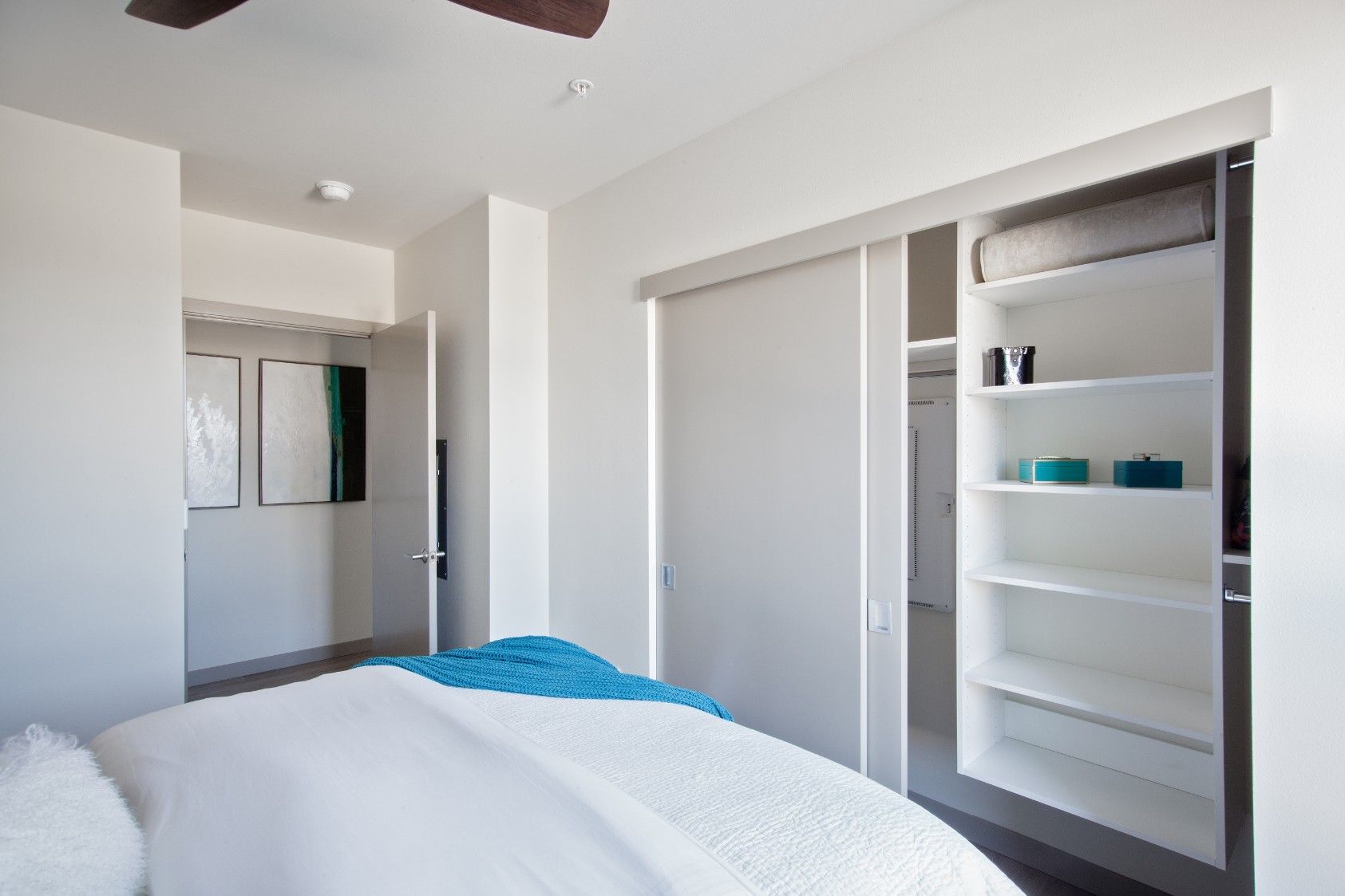 Bright bedroom with white walls, bed, mirrored closet, and open shelving alcove