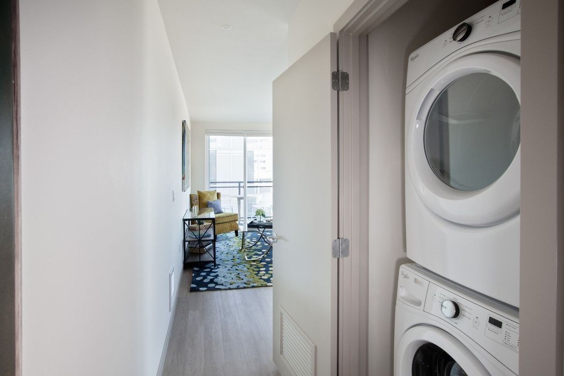 Hallway with stacked washer and dryer on the right, leading to a bright room with a table and chairs.
