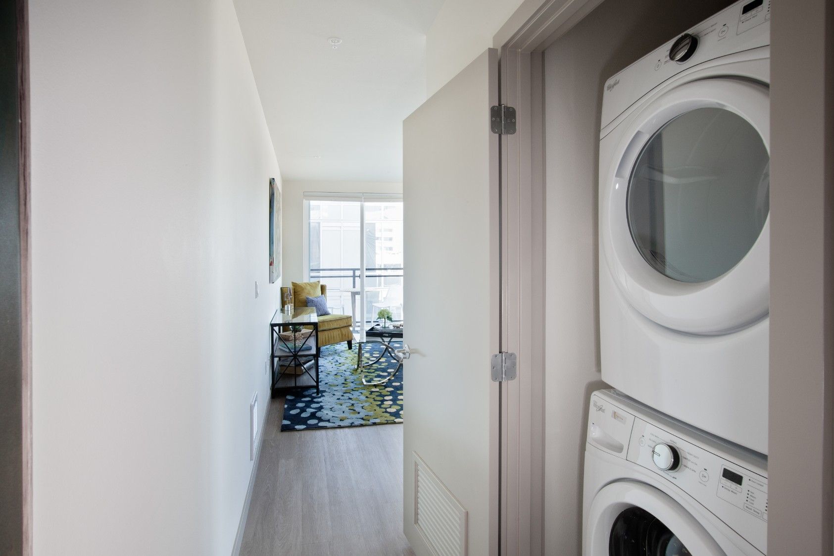 Hallway with stacked washer and dryer on the right, leading to a bright room with a table and chairs.