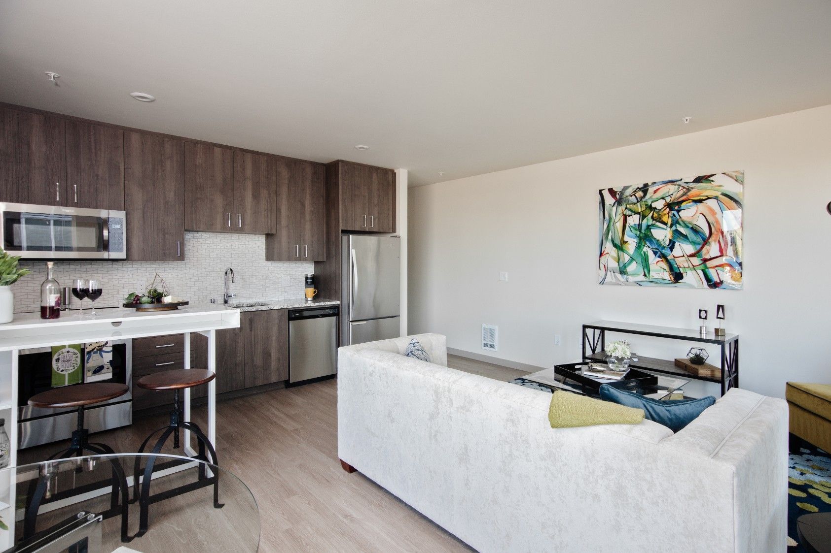 Bright modern studio apartment with kitchen, dining table, white sofa, and abstract wall art