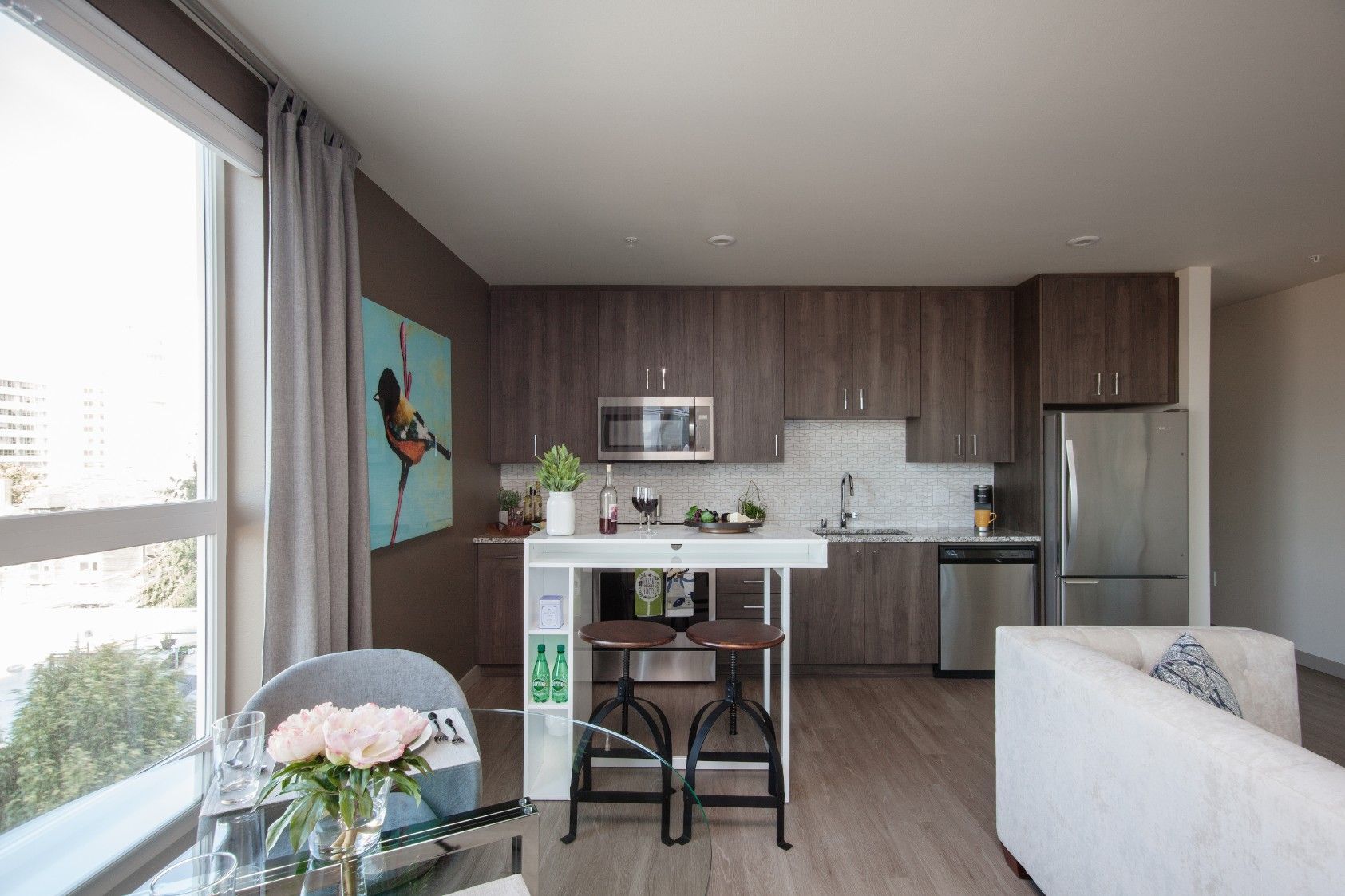 Modern open-plan kitchen and living room with gray cabinets, island, large window, and dining stools