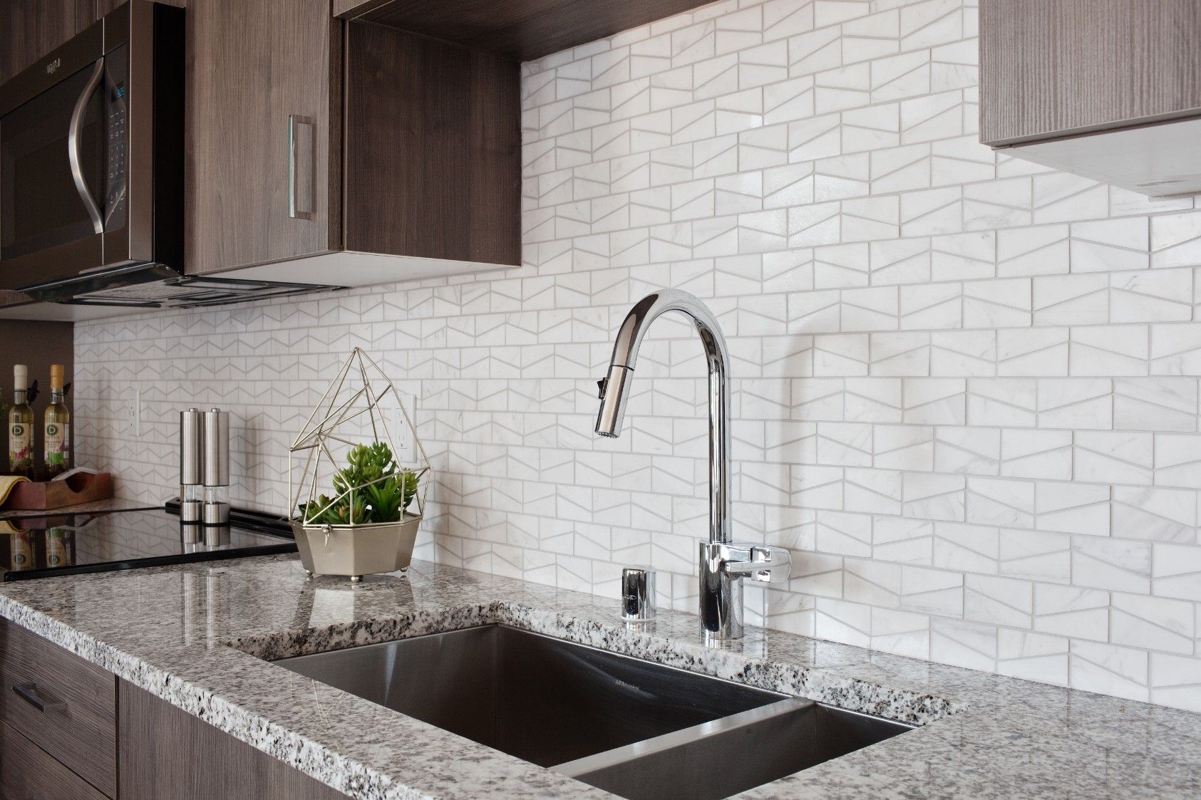 Modern kitchen sink with granite countertop, chrome faucet, and white subway tile backsplash