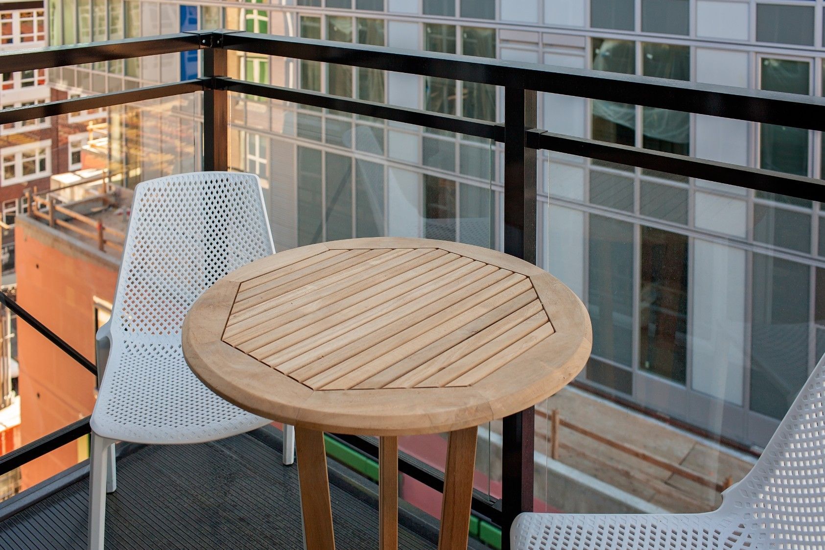 Small balcony with a round wooden table and two white chairs overlooking a city view