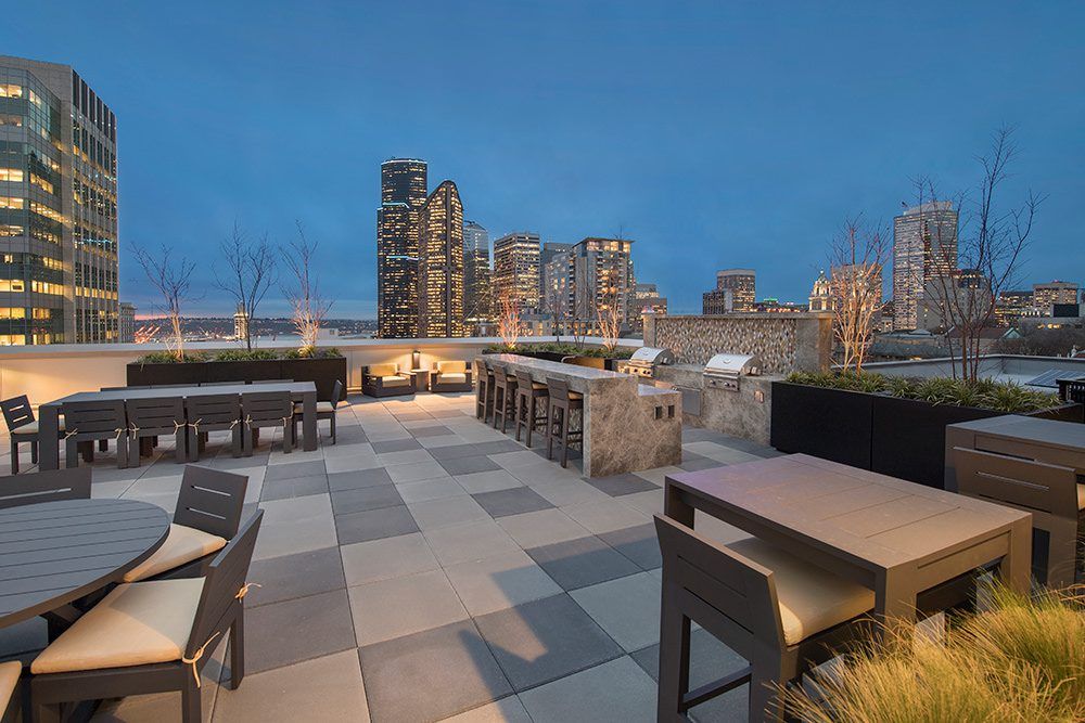 Rooftop terrace with lounge seating, checkerboard tiles, and city skyline at dusk