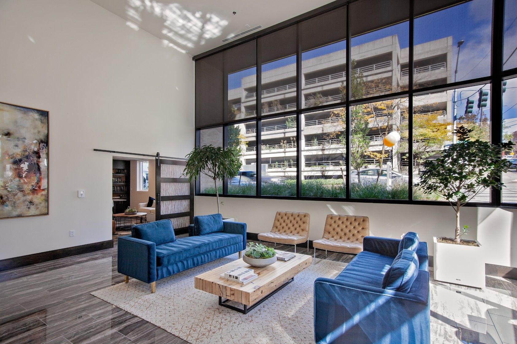 Modern lobby lounge with blue sofas, coffee table, and large windows overlooking a city building.