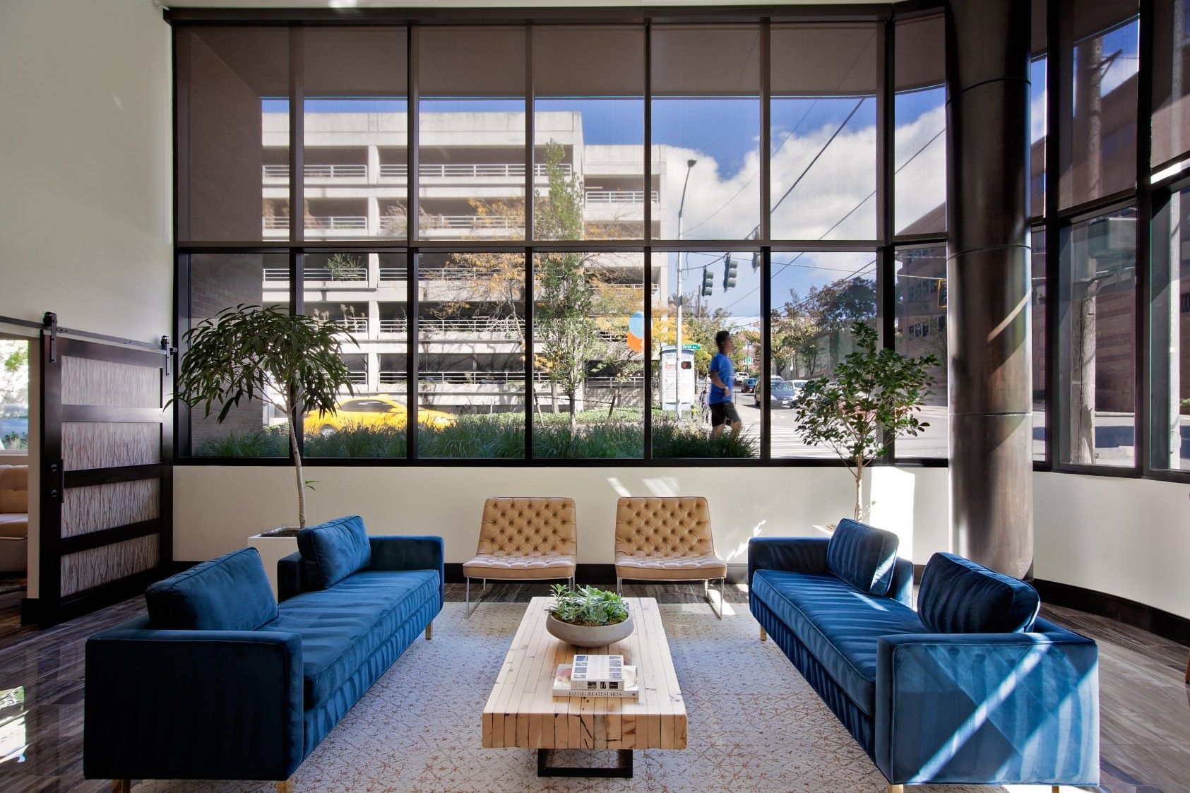 Modern lobby with blue sofas, coffee table, and large windows overlooking a building and sky