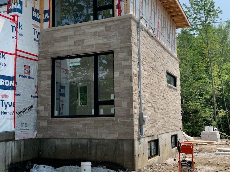 Une maison est en construction avec une façade en briques et beaucoup de fenêtres.