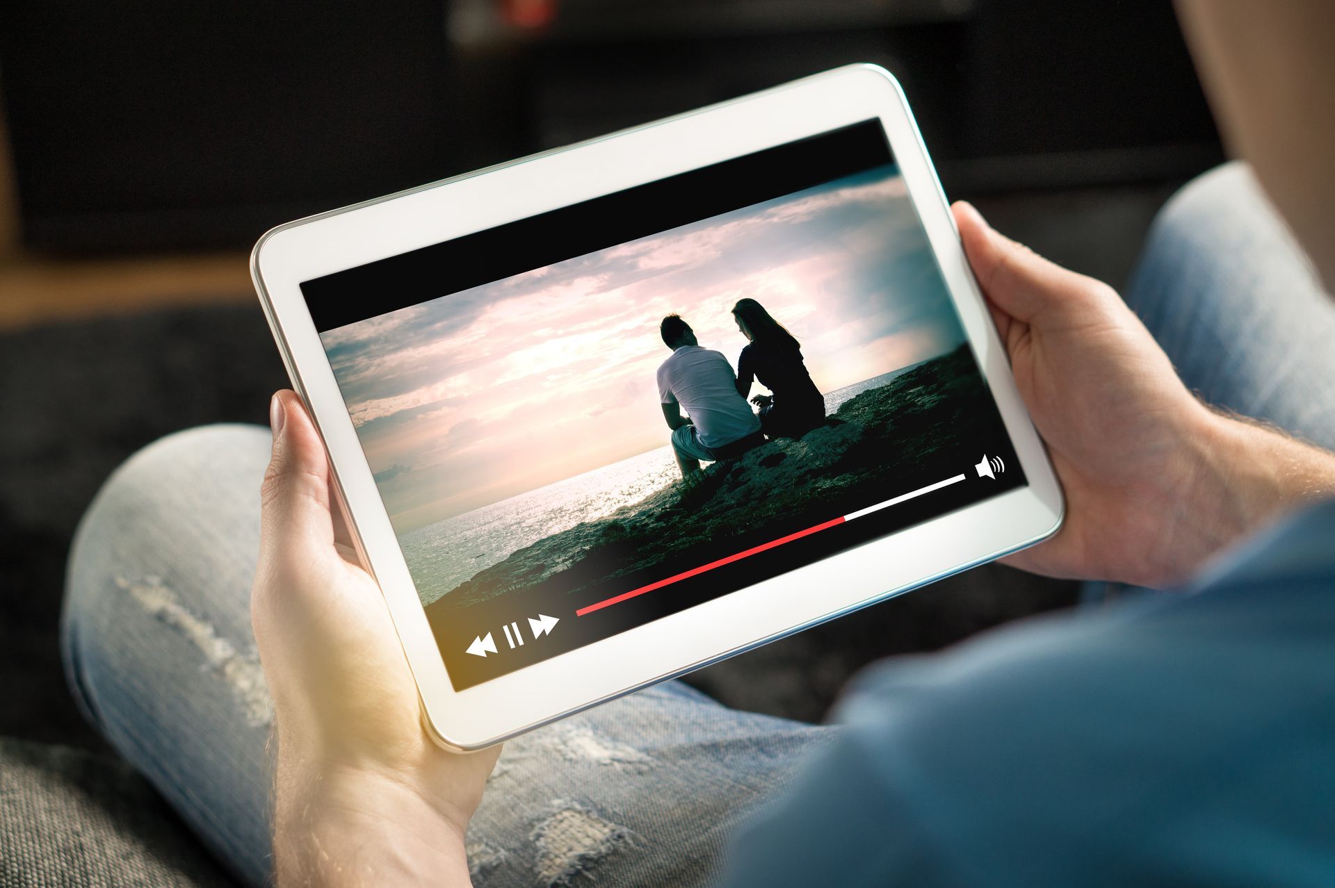 Person watching a video on a tablet. Screen shows two figures, sitting outdoors.