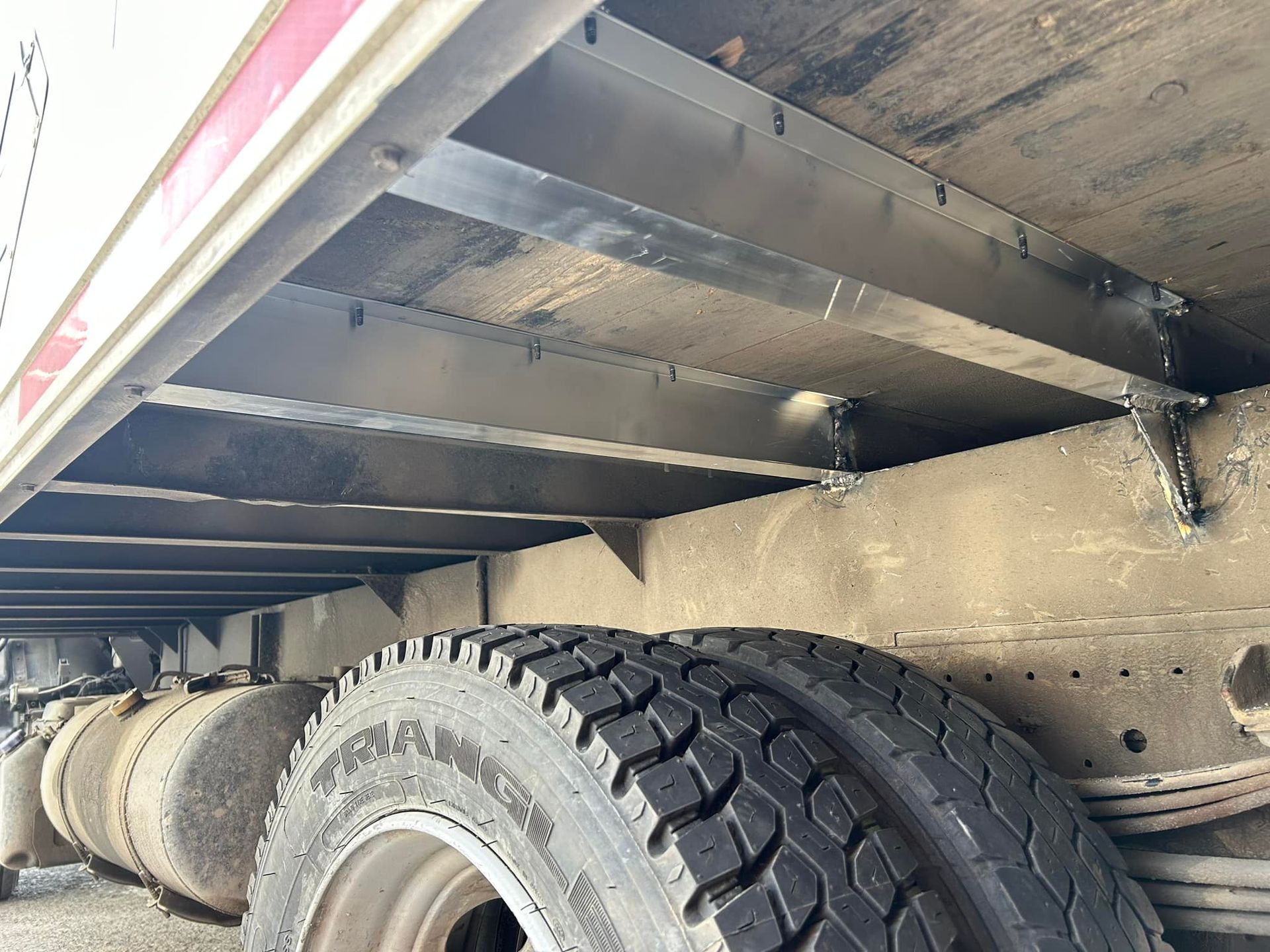 Châssis d'une remorque de camion, montrant les supports métalliques, le pneu et l'accumulation de saletés.