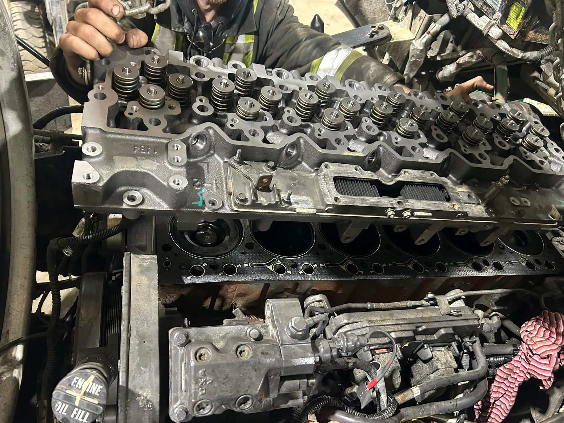 Un mécanicien travaille sur un moteur démonté, probablement celui d'un camion, en se concentrant sur la culasse. Ses mains sont visibles.