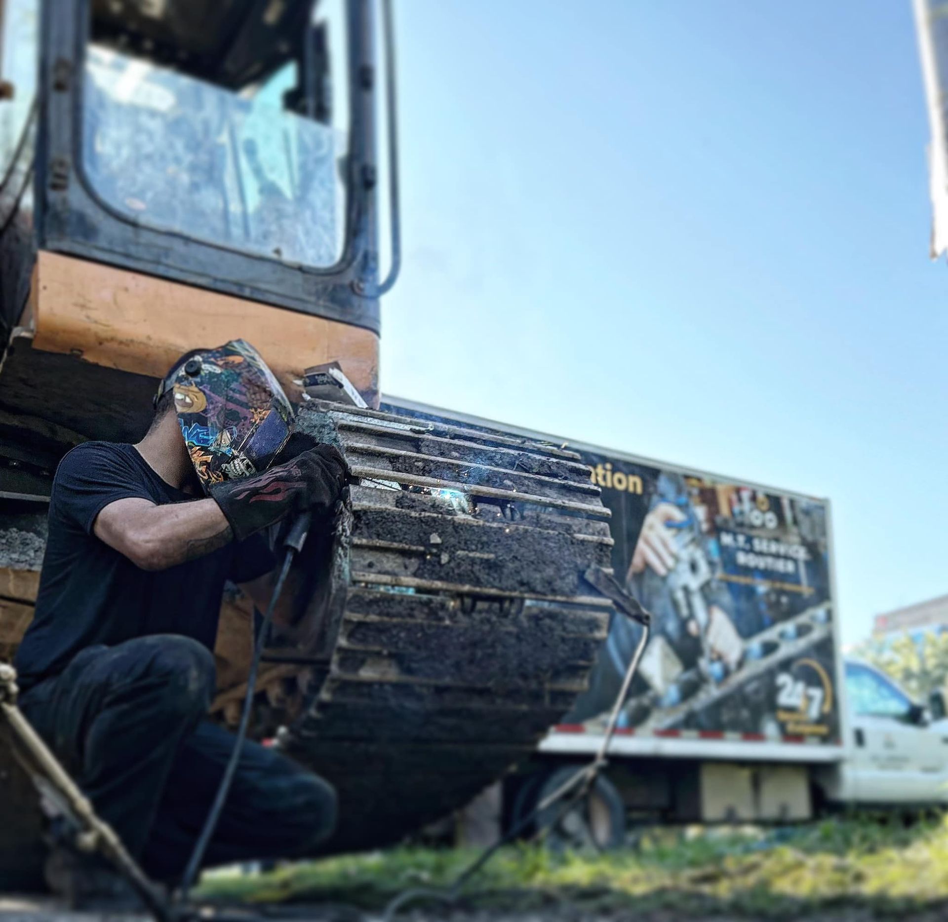 Une personne soude sur un gros engin de chantier à l'extérieur.