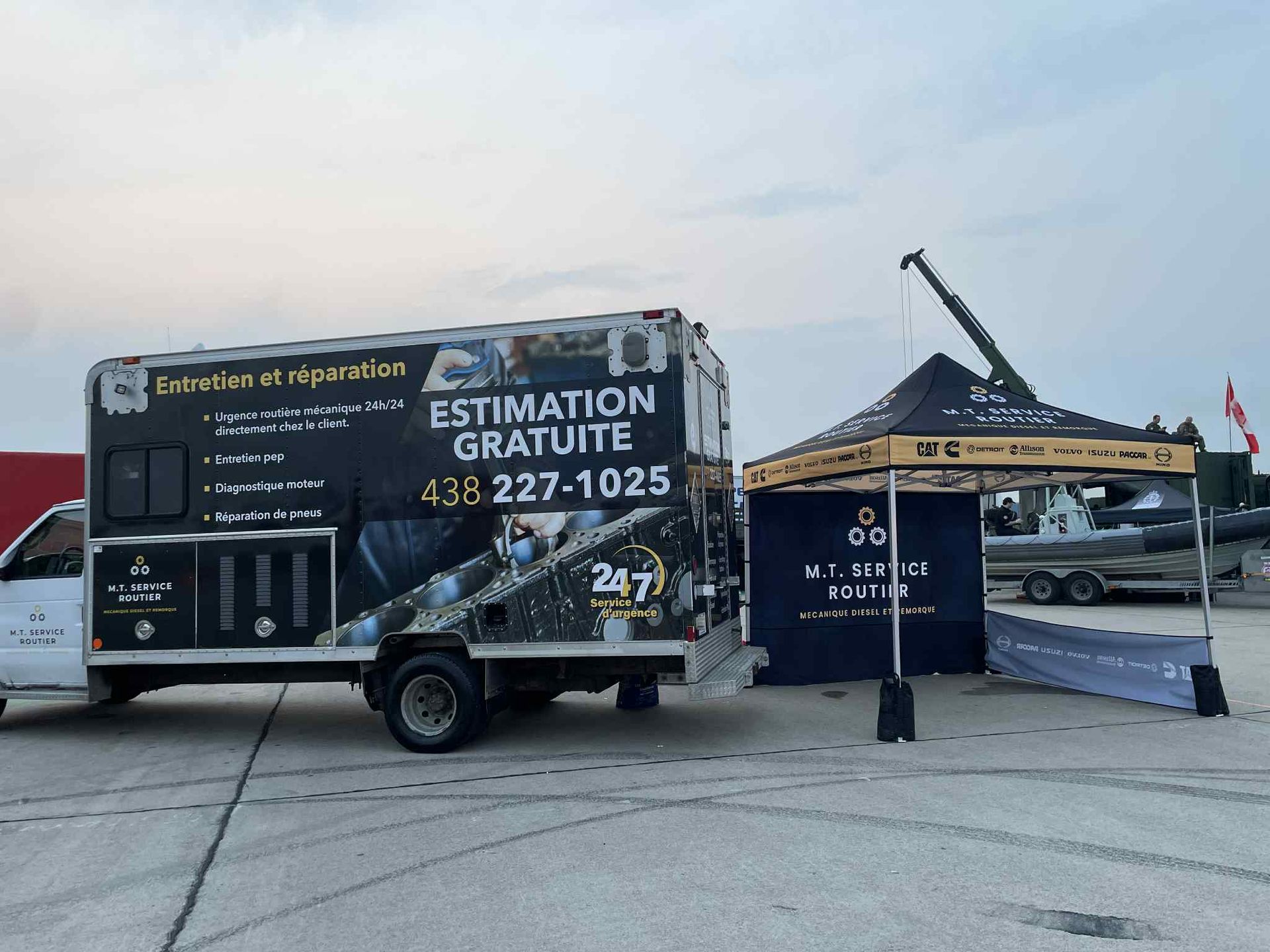 Un camion de travail blanc avec un panneau « Estimation Gratuite » à côté d'une tente noire portant le logo de l'entreprise.