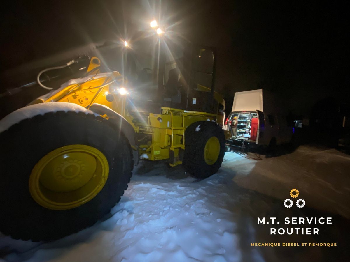 Un tracteur jaune est garé dans la neige la nuit.
