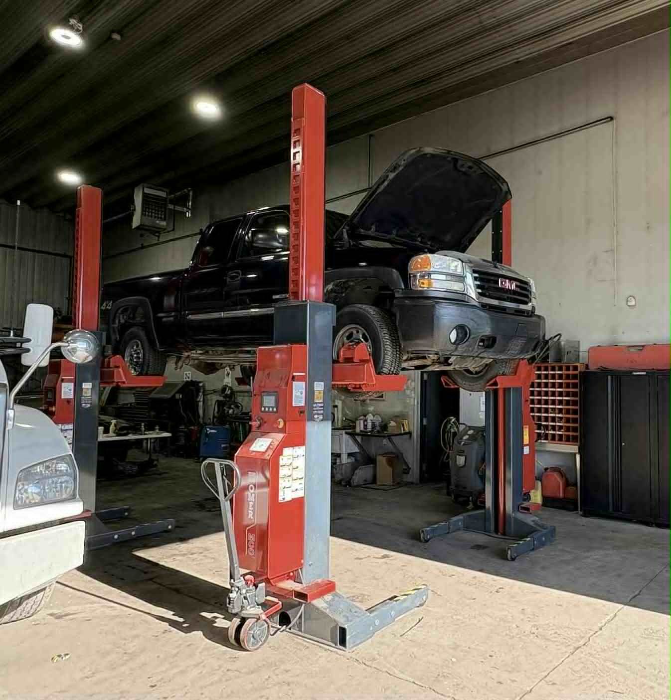 Camion noir soulevé sur un pont élévateur rouge à l'intérieur d'un garage.