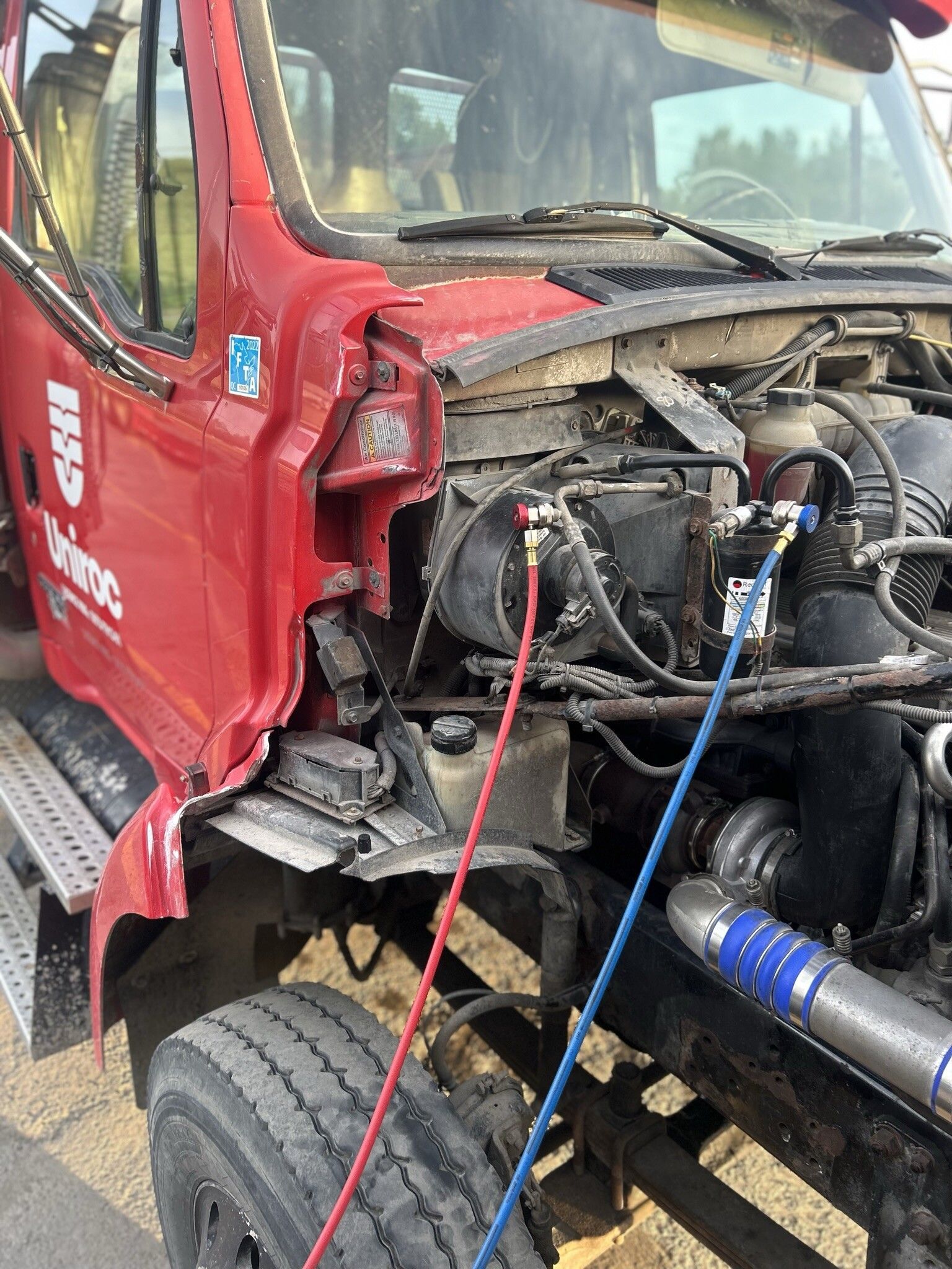 Un camion rouge avec le capot ouvert et un tuyau attaché dessus.