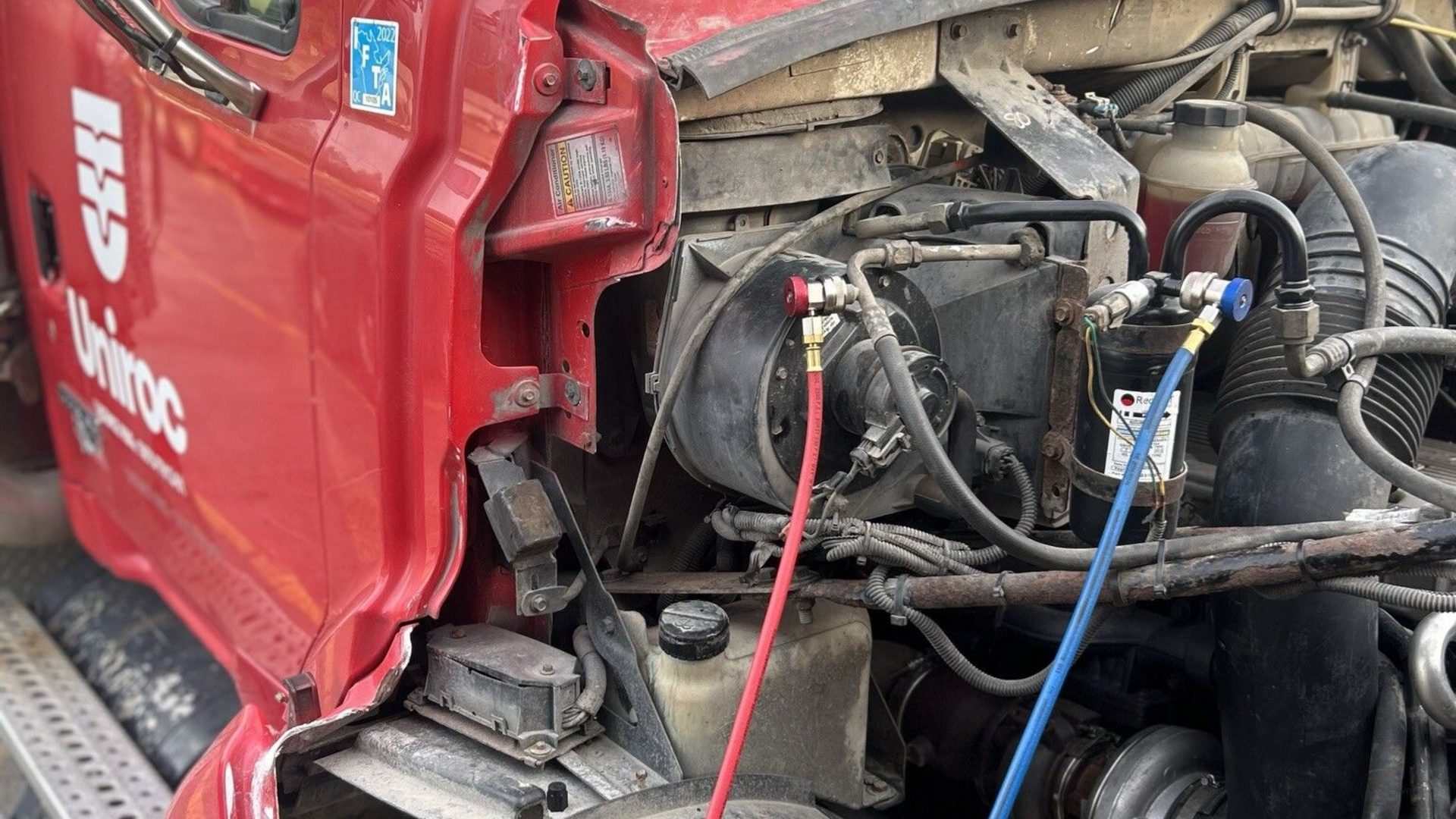 Avant endommagé d'un camion rouge, moteur et câbles apparents, probablement suite à un accident ou une réparation.