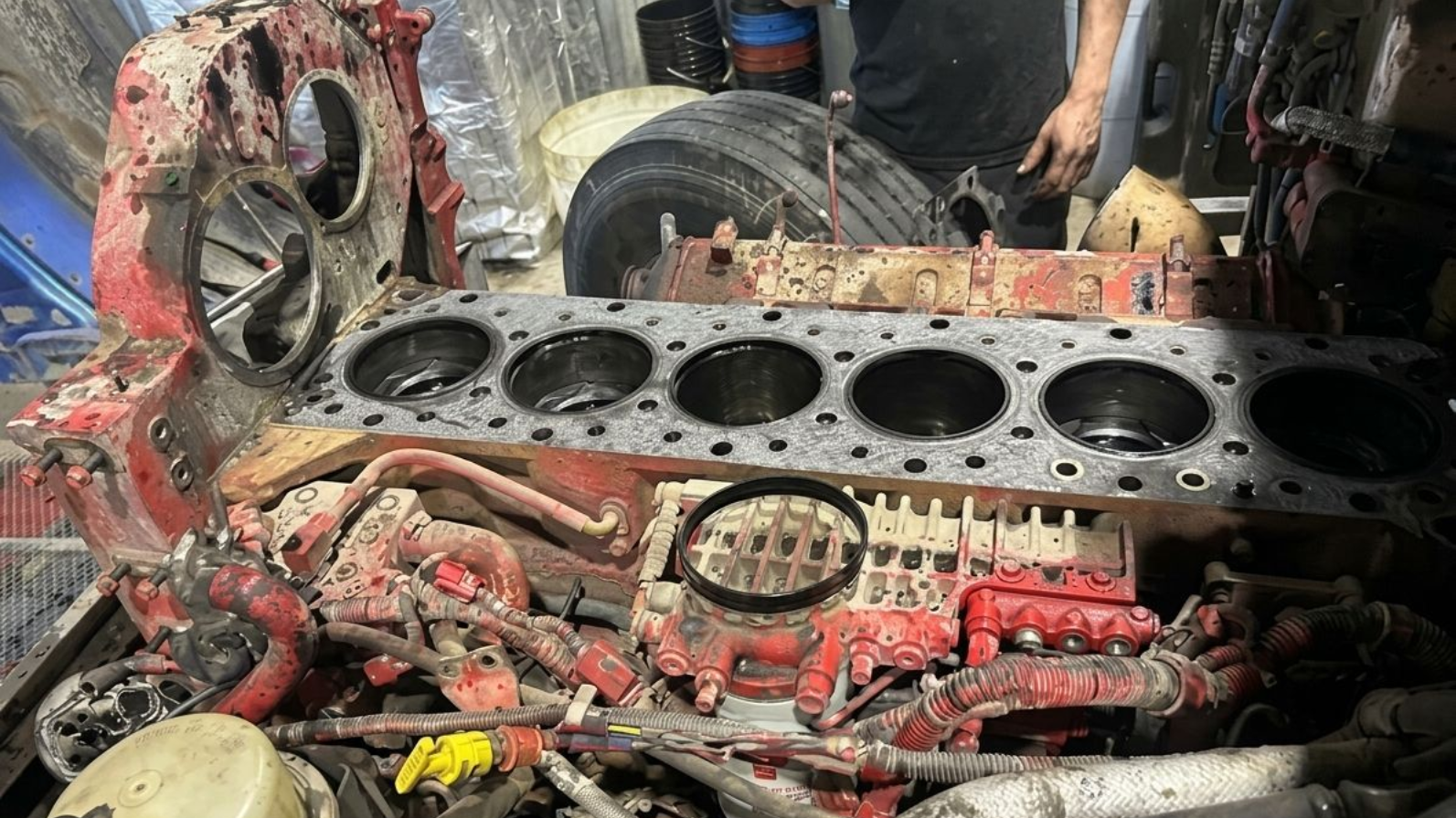 Compartiment moteur endommagé d'un camion rouge, avec tuyaux et câbles apparents, vu de côté pendant les réparations.