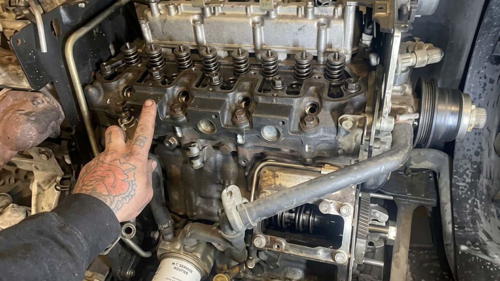 Compartiment moteur endommagé d'un camion rouge, avec tuyaux et câbles apparents, vu de côté pendant les réparations.