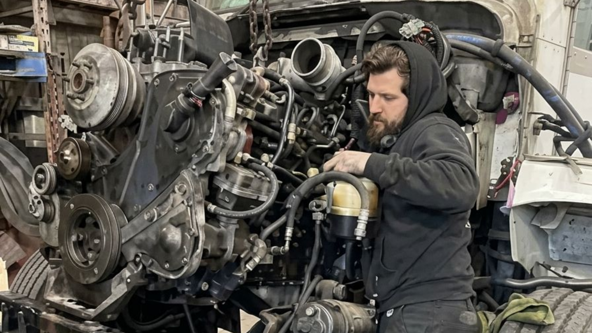 Une personne est agenouillée à côté d'un grand filtre à air cylindrique posé sur le sol d'un atelier.