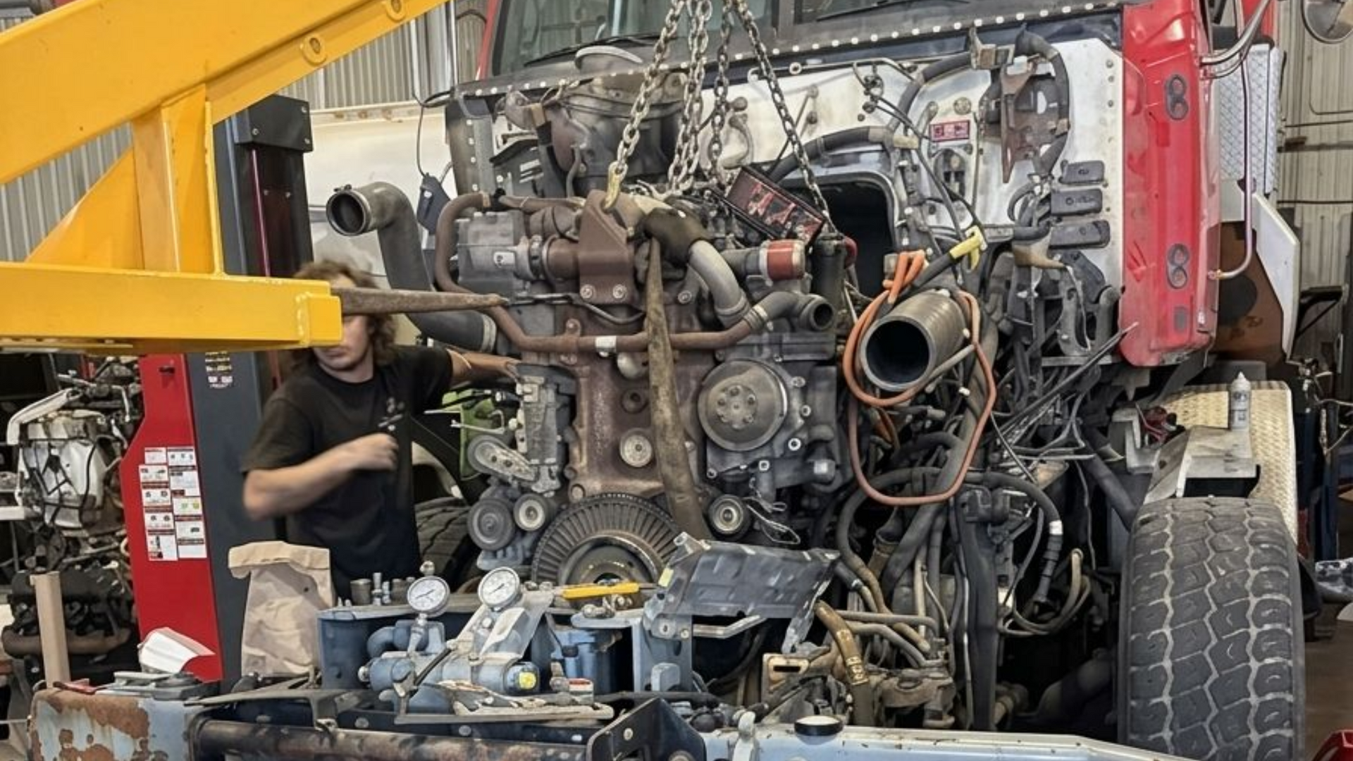 Une personne est agenouillée à côté d'un grand filtre à air cylindrique posé sur le sol d'un atelier.
