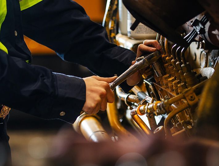 Un mécanicien travaille sur un moteur à l'aide d'une clé. Détails : mains, vêtements jaunes et bleu marine.