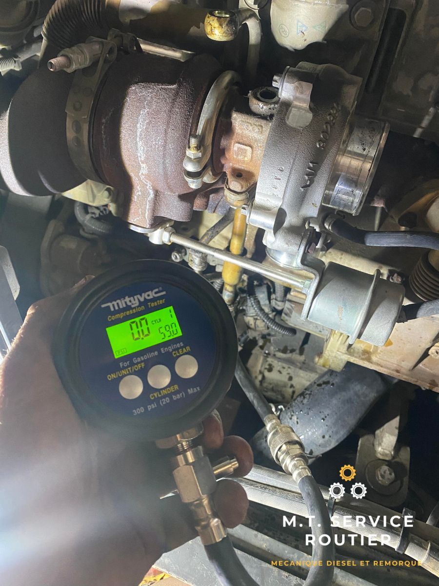 Une personne tient une jauge numérique devant un turbocompresseur.