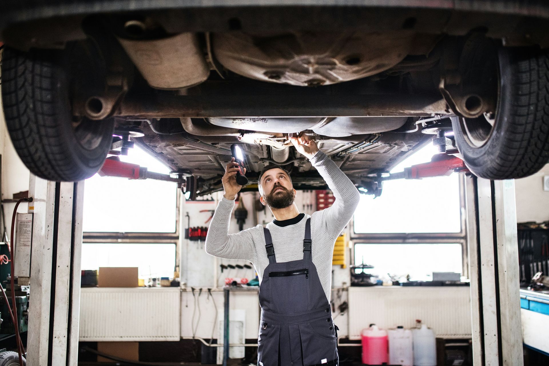 A man is working under a car on a lift in a garage.