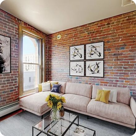 Living room with brick walls, a pink sectional sofa, and framed art. Sunflowers on coffee table.