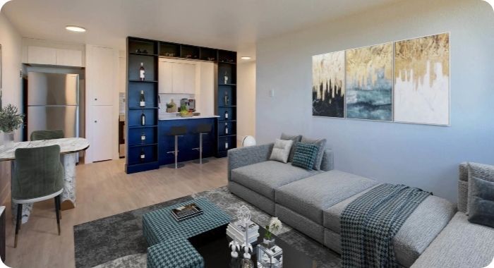 Modern living room with gray sofa, navy bar nook, abstract wall art, and dining table near a window.