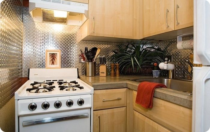 Compact kitchen with white stove, wood cabinets, tiled backsplash, and a red towel on the counter