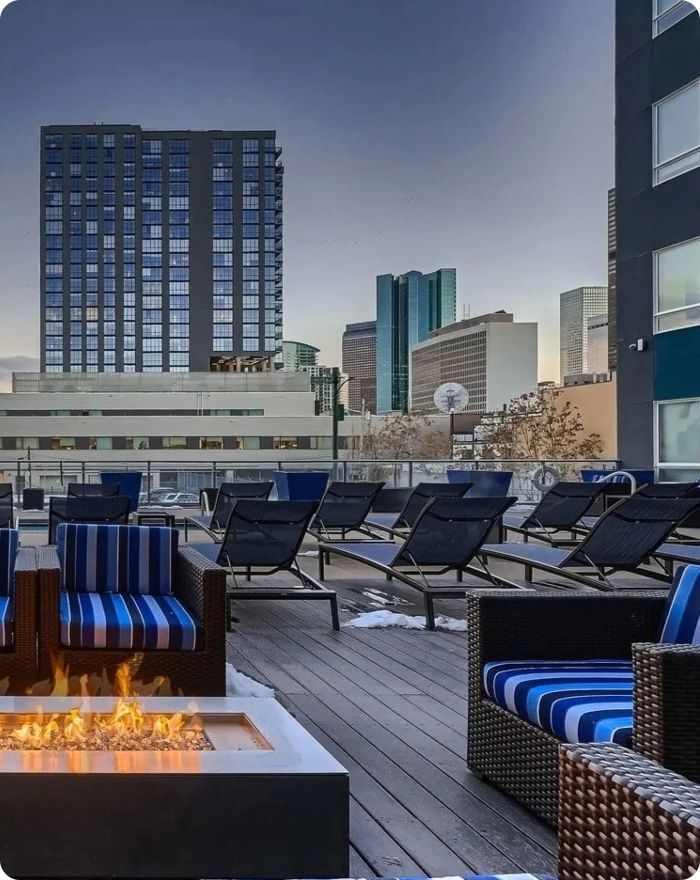 Rooftop patio with fire pit and striped lounge chairs overlooking a city skyline at dusk