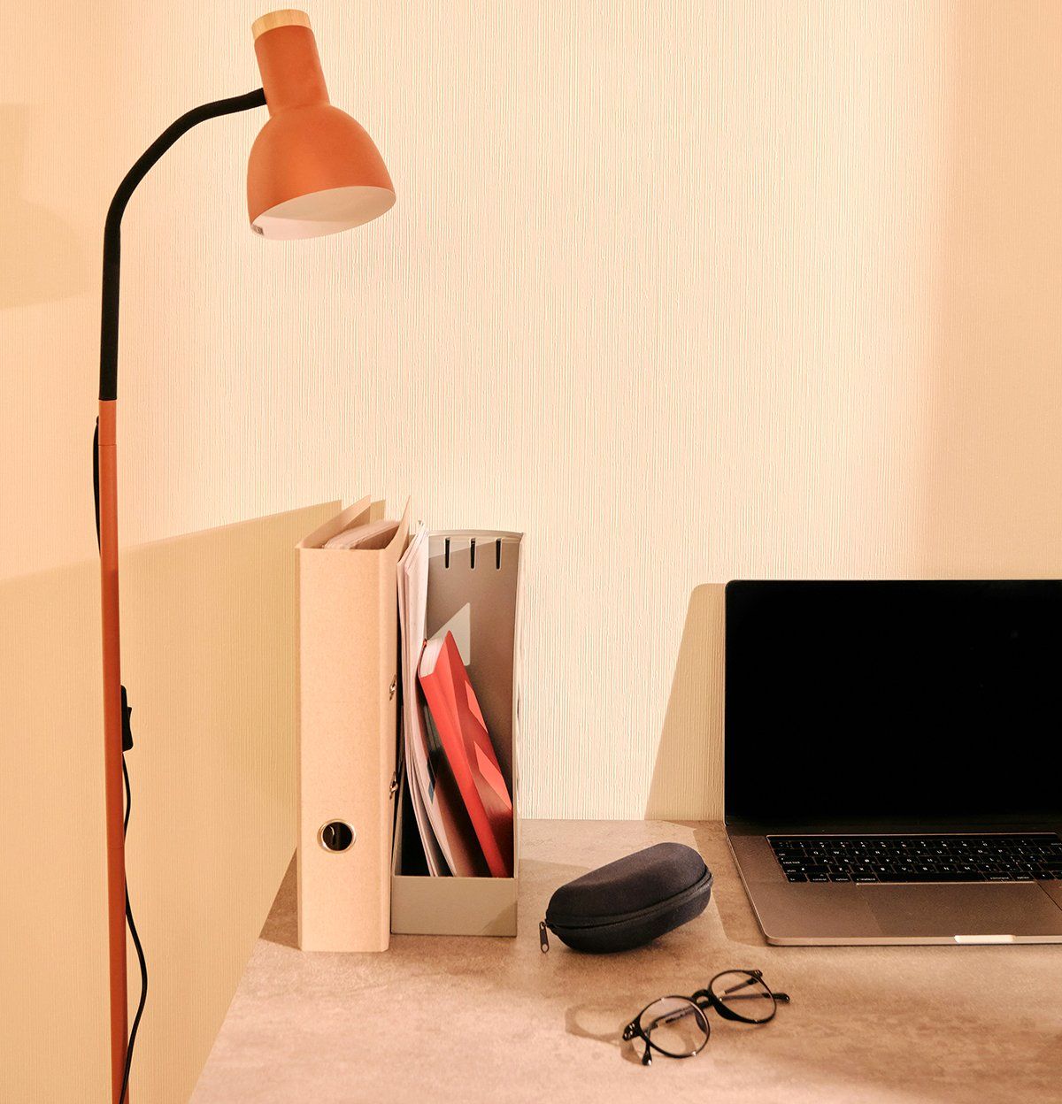 Cozy desk with orange lamp, books, laptop, glasses, and a potted plant on a wooden shelf above.