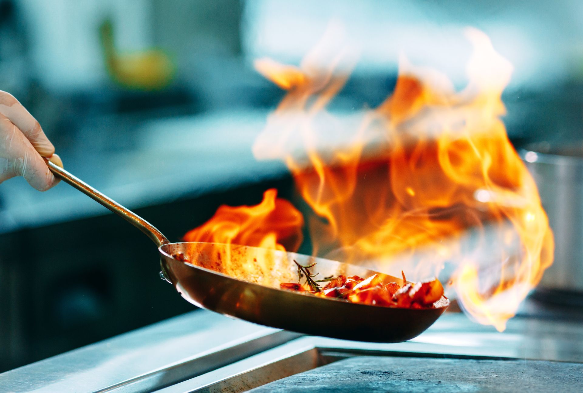Chef flambéing vegetables in a skillet with open flames in a restaurant kitchen