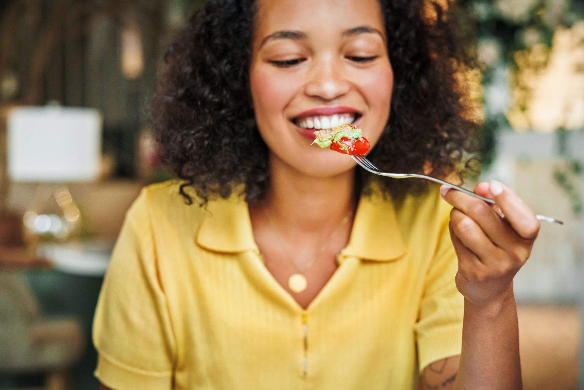 Young lady with a yellow shirt smiling about to eat tomato and salad Young lady with a yellow shirt smiling about to eat tomato and salad