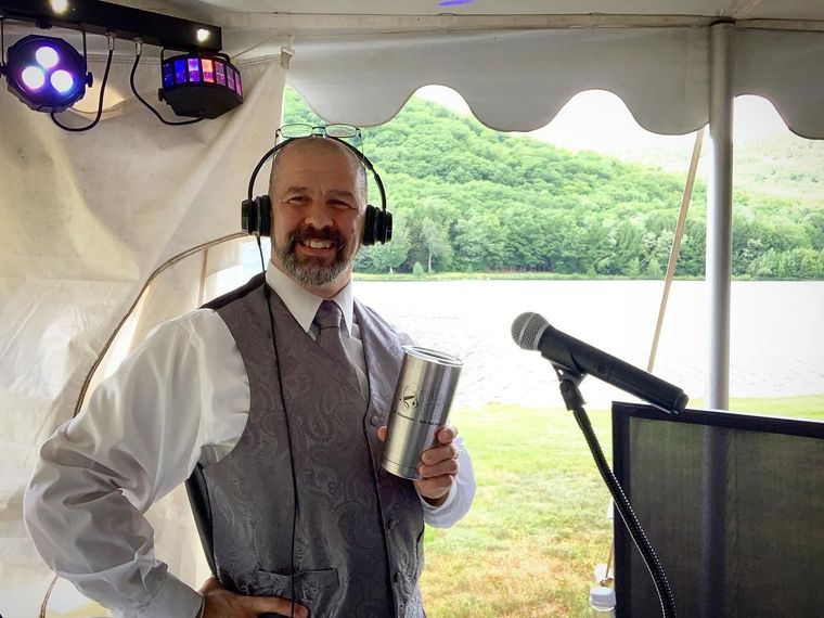 DJ at an event dressing in formal attire, holding his Mix It Up! coffee tumbler, with his head set on and microphone in front of him.