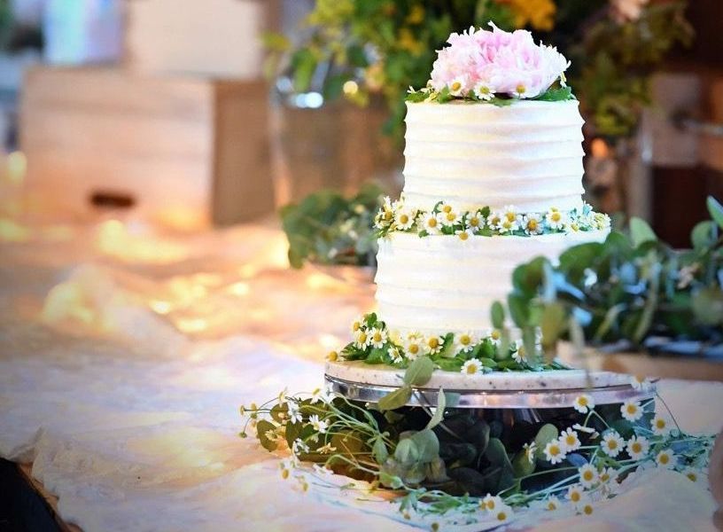 2-tiered, 4-layers per tier, finished wedding cake on display with several small daisies decorating around where the cake tiers meet.