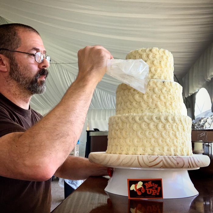 DJ decorating a 3 tier cake with white swirled frosting