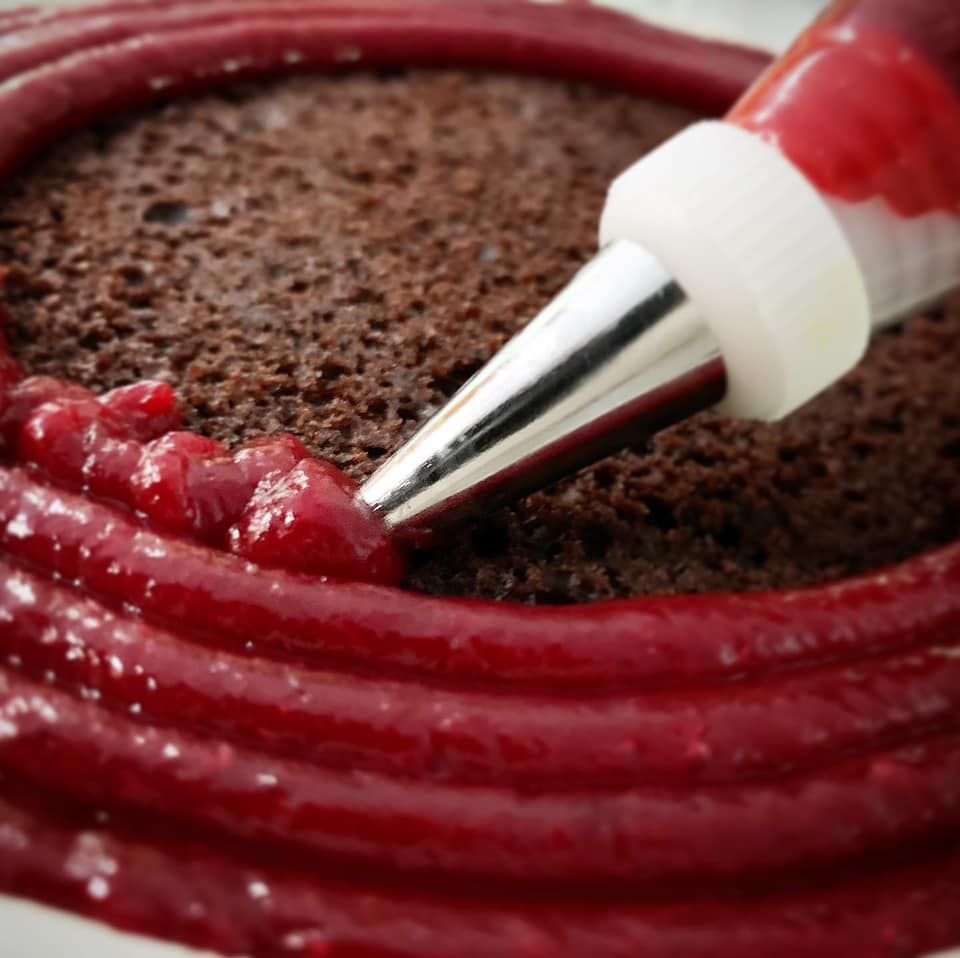 Raspberry filling being piped onto a layer of chocolate cake for its filling.