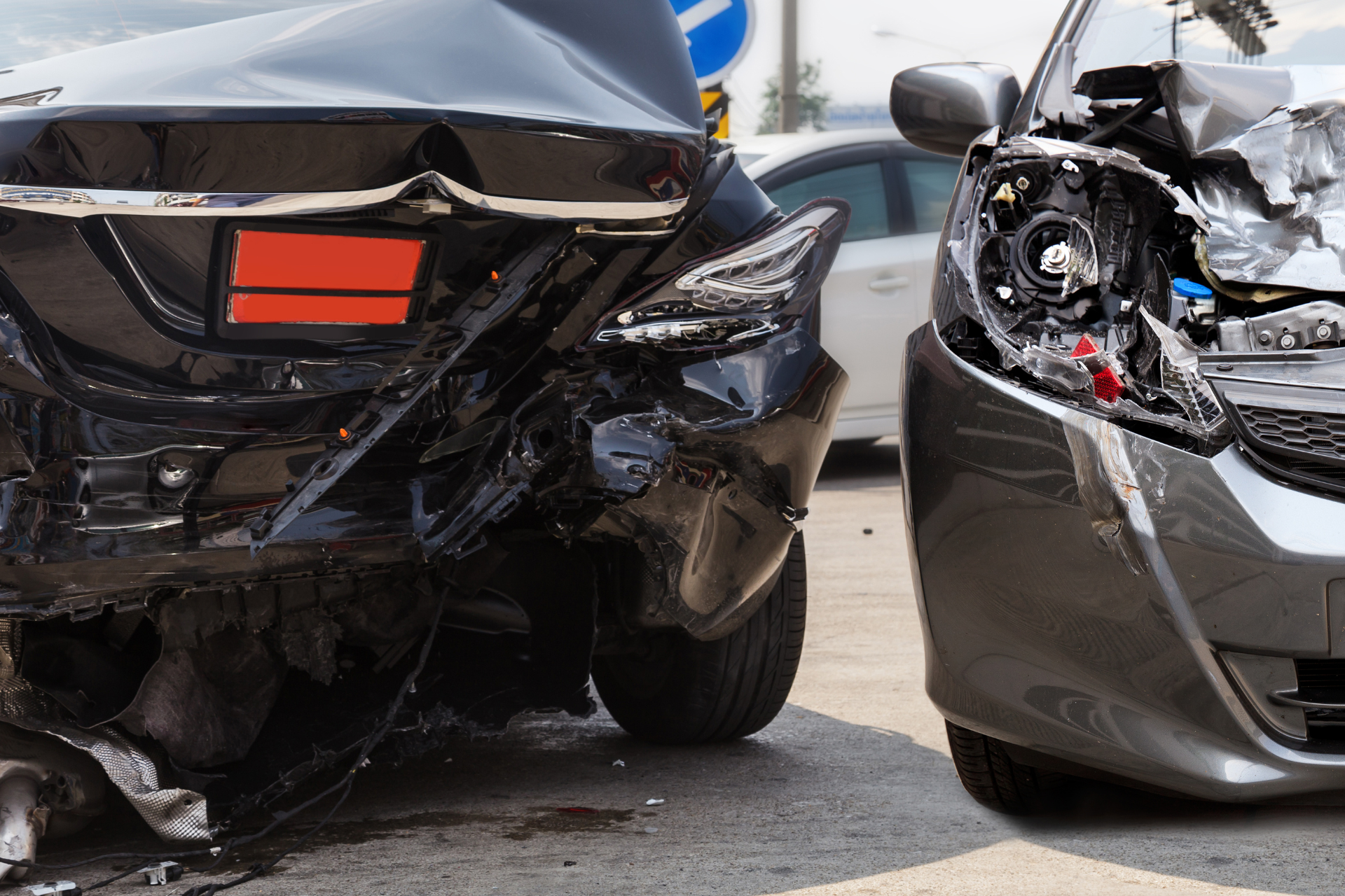 Two cars with heavy front-end crash damage, black car facing a silver car in a parking lot.