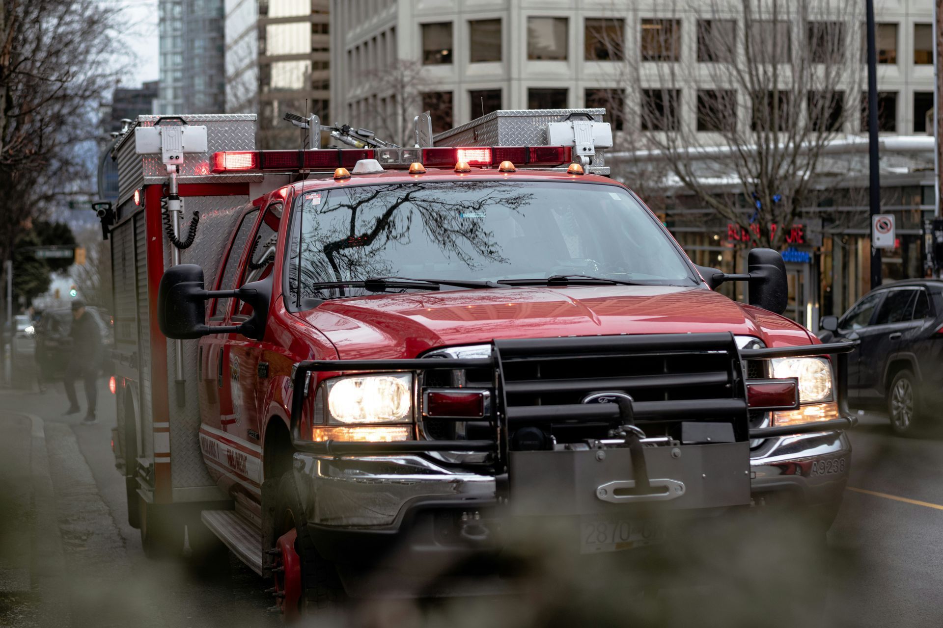 Red emergency vehicle with flashing lights driving through a city street