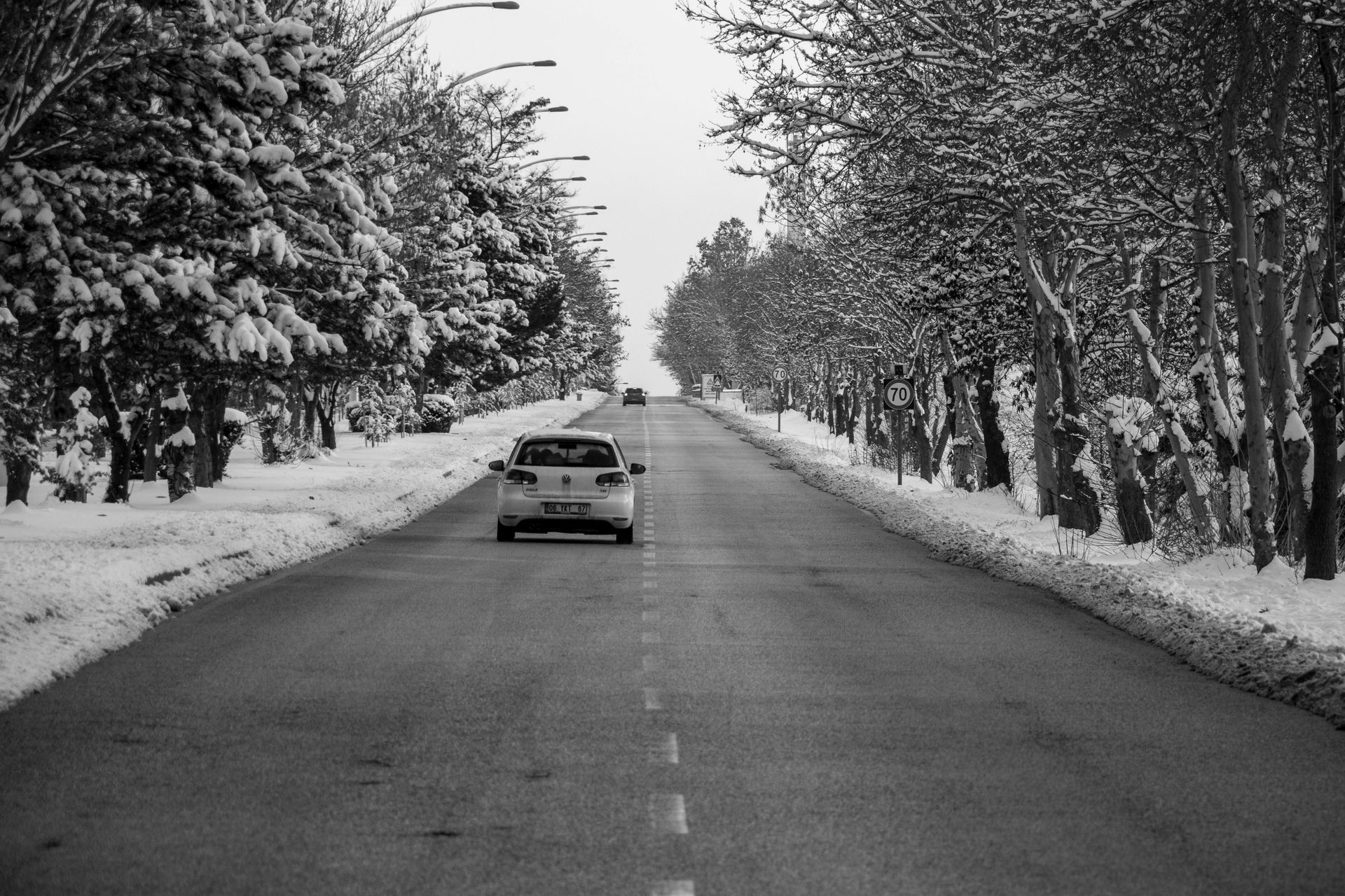 Snowy road with a car driving away between snow-covered trees