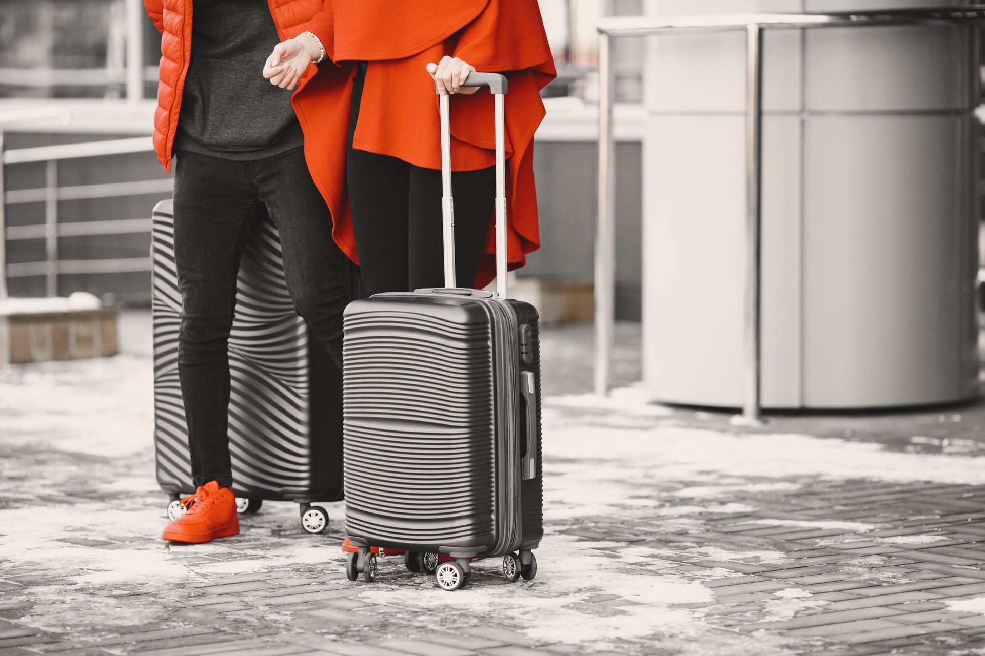 Two people standing with a striped carry-on suitcase in an airport or transit terminal