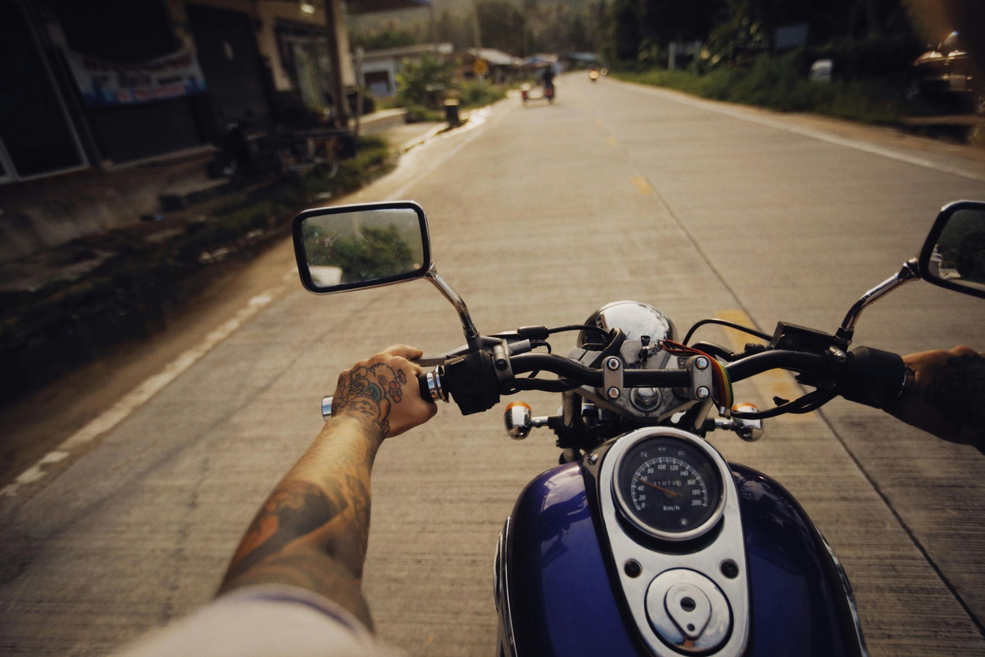 Rider’s view from a motorcycle on a sunlit road, hands on handlebars and mirror visible