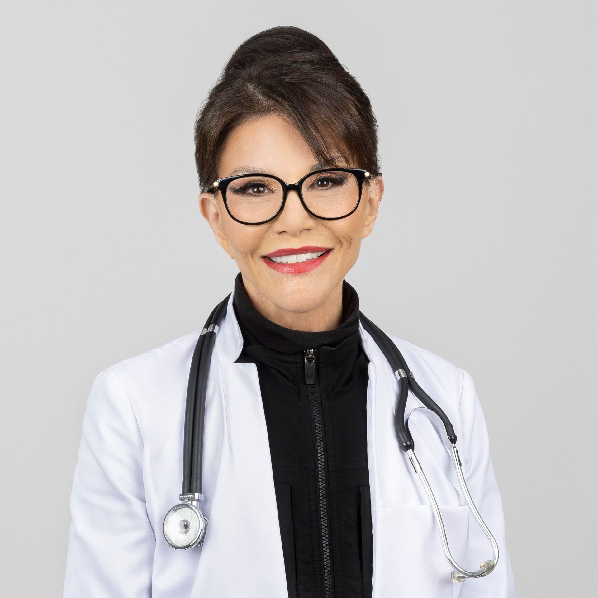 A female doctor wearing glasses and a white coat with a stethoscope around her neck.