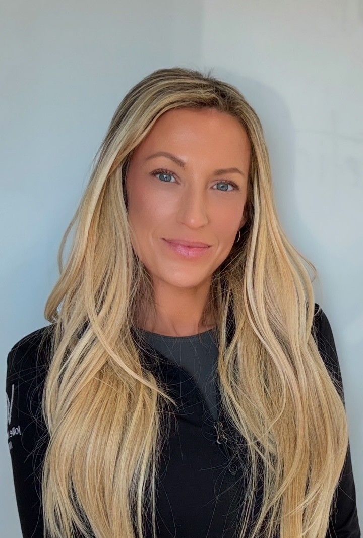 A woman with long blonde hair is wearing a black jacket and smiling for the camera.
